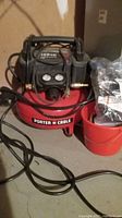 Full view of the red Porter Cable air compressor with hose and bucket of attachments beside it