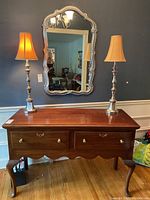 Full front view of the black cherry buffet with two silver lamps on top and a wall mirror behind.