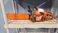 Orange Husqvarna 350 chainsaw placed on a plastic shelf, showing the full side profile with the chain covered by the sheath.