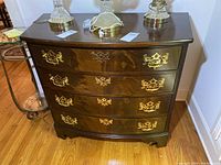 Front view of curved front wooden chest showing four drawers with brass handles and keyhole covers on wooden floor.