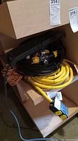 Three coiled cords in a wooden box: a heavy-duty black cord with yellow connectors, a yellow cord, and an orange cord underneath.