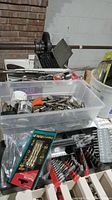 Photo showing a large plastic container filled with a variety of drill heads and drill bits of different sizes and types, including hole saw bits and taps.