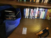 Photo showing DVDs and VHS tapes in a blue bag and on a wooden surface with some books in the background.