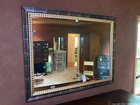 Full view of large rectangular wall mirror with dark faux crack frame, gold ridged inner frame, reflecting furniture and room interior.