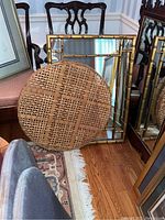 Photo showing rectangular faux bamboo framed mirror leaning against wall with round rattan woven wall art in front on hardwood floor.