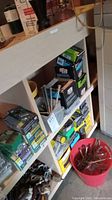 Boxes of nails and screws on wooden shelf, some boxes stacked and in good condition. Red bucket on floor with loose nails and screws.