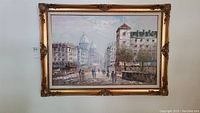 Full front view of framed oil painting showing cityscape scene and ornate gold frame