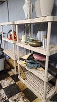 Two beige plastic shelving units with multiple tiers, showing some dirt and outdoor use. Various unrelated items are on the shelves but not included.