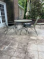 Full view of wrought iron table and three chairs set on a stone patio with umbrella in hole