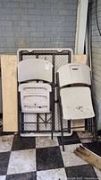 Photo of folded Lifetime outdoor table, two folding chairs, wooden pallet, and metal poles stacked against wall.
