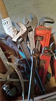 Photo showing collection of large wrenches, pliers including locking pliers, and hammer with wooden handle inside a container.