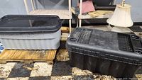 Two large plastic storage totes stacked, one black and one gray, both showing signs of dirt and dust.
