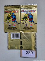 Photo showing three sealed 1991 O-Pee-Chee Premier hockey card packs in gold foil with graphics of two hockey players, front and back views.