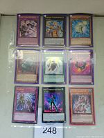 Photo of nine Yu-Gi-Oh! holographic cards arranged in a 3x3 grid inside plastic sleeve page protector.