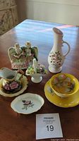 Table display of seven porcelain pieces with floral themes and figurines