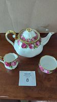 Tea set including teapot, creamer, and sugar dish showing floral design and gold accents.