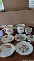 Set of 2 tea cups, 4 saucers and 2 small bowls with floral patterns arranged in front of a cardboard box