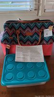 Photo showing colorful Arctic Zone insulated picnic satchel bag with brown leather handles and a large turquoise plastic food container with circular indentations on the lid.