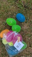 Six assorted colored spiked rubber dog balls inside a plastic bag displayed on grass