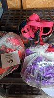Photo showing three bundles of dog leashes and harnesses in pink, purple, and orange colors placed on a metal surface.