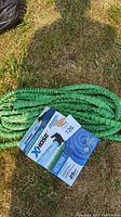Green expandable garden hose and blue XHose garden hose in original packaging on grass.