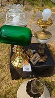 Photo of three vintage lamps showing green banker's lamp with brass base, decorative lamp with etched floral glass shade, and small lamp with frosted glass base and clear chimney.