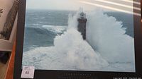 Framed wall art showing a dramatic black and blue photo of a lighthouse being hit by large waves during a storm.