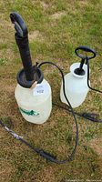 Photo of two handheld garden sprayers on grass surface, showing their containers, pump handles, and spray wands.
