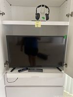 33.5-inch Roku television with two remote controls in front, wireless headset on shelf above, all inside a white cabinet.