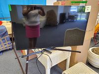 Front view of the Samsung 44-inch TV on a TV stand with cables visible underneath; reflective screen shows partial reflection of photographer and room.