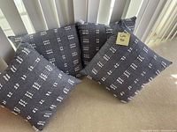 Four gray square accent pillows with white woven linear pattern arranged on a chair.