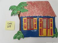 Photo of handcrafted colorful artwork depicting a blue house with red roof and yellow-red windows, next to a palm tree and plants.