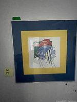 Photo shows framed artwork featuring two fish with a double mat (yellow and blue) in a square frame against a wall.