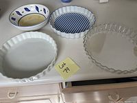 Four assorted pie and quiche plates on a white countertop: white ceramic, blue and white ceramic with pattern, white ceramic fluted tart dish, clear glass fluted pie plate.