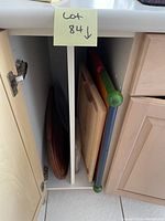 Photo showing five assorted kitchen cutting boards stored vertically in a kitchen cabinet. Boards include wooden and composite types with varied sizes and shapes.