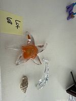 Close-up top angle of glass starfish with orange center, dolphin figurine, and shell piece on white surface.