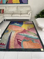 Photo of the rectangular contemporary area rug placed on a tiled floor between white furniture, showing the colorful abstract geometric design and overall condition.