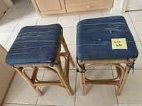 Two cushioned counter stools with blue fabric cushions on light rattan/wicker style wooden frames viewed from top and angle.