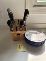 Wooden cutlery block holding five knives of different sizes and a stack of six round ceramic dishes with colorful star patterns around the rim.