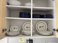Photo of dishware inside a cabinet including stacks of plates and bowls with a blue and white animal design, navy blue bowls, and two large white serving bowls on the top shelf.