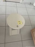 Top view of small white folding end table showing circular surface and carrying hole.