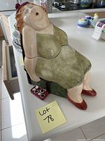 Photo of ceramic cookie jar shaped as a seated woman in green dress and red shoes.