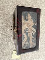 Closed jewelry box showing top with painted landscape and brass latch