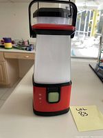Front view of red and black Coleman LED lantern on kitchen counter with visible handle and power button.