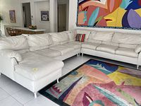 Large white sectional sofa with chaise, corner, and armless sofa sitting in a living area with colorful wall art and rug.