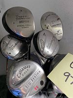 Close-up of metal golf club heads showing brand names and numbers including Tiger Power Super 3, King Cobra 1 and 3, Callaway Big Bertha