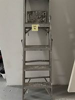 Front-facing photo of a 5-foot metal ladder with four steps and platform top. Surface shows wear and paint stains.