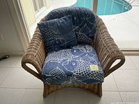 Rattan chair with blue fish-patterned cushions shown from front angle on patio beside a pool.