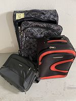 Four assorted suitcases and travel bags grouped together against a white wall.