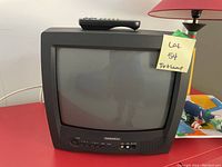 Front view of Daewoo small CRT television with remote on top, sitting on red table.